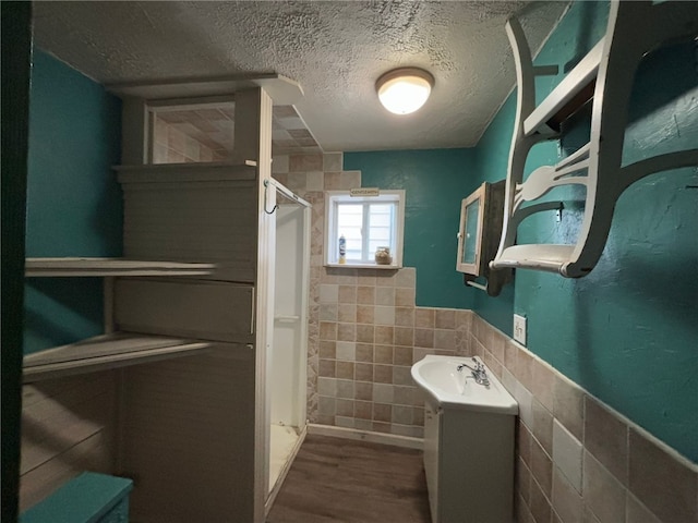 bathroom with walk in shower, vanity, a textured ceiling, wood-type flooring, and tile walls