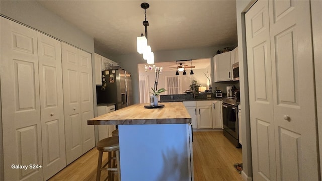 kitchen with white cabinetry, wooden counters, a center island, a kitchen breakfast bar, and stainless steel appliances