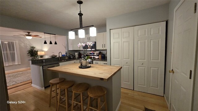 kitchen with white cabinetry, a center island, wooden counters, decorative light fixtures, and appliances with stainless steel finishes