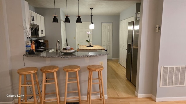 kitchen with decorative light fixtures, dark stone countertops, stainless steel fridge, light hardwood / wood-style floors, and kitchen peninsula