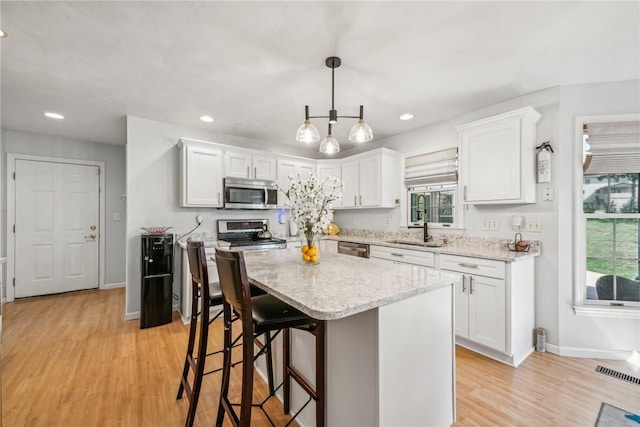 kitchen featuring a center island, white cabinets, light hardwood / wood-style flooring, appliances with stainless steel finishes, and decorative light fixtures