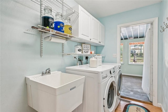 clothes washing area with light hardwood / wood-style flooring, cabinets, sink, and washing machine and clothes dryer