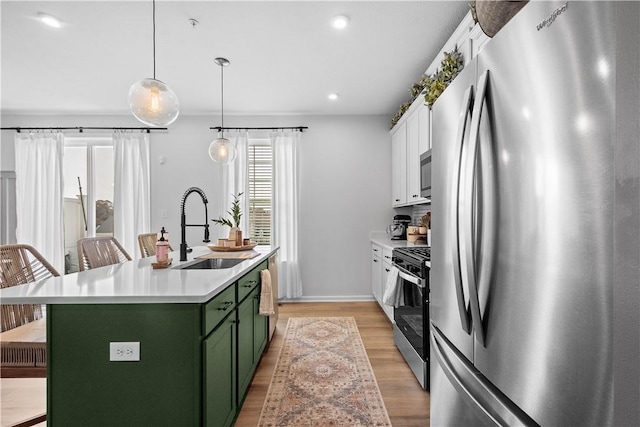 kitchen featuring stainless steel appliances, a kitchen island with sink, sink, white cabinetry, and hanging light fixtures