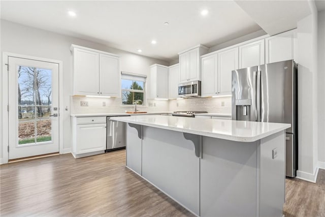 kitchen with hardwood / wood-style floors, stainless steel appliances, a kitchen island, and white cabinetry