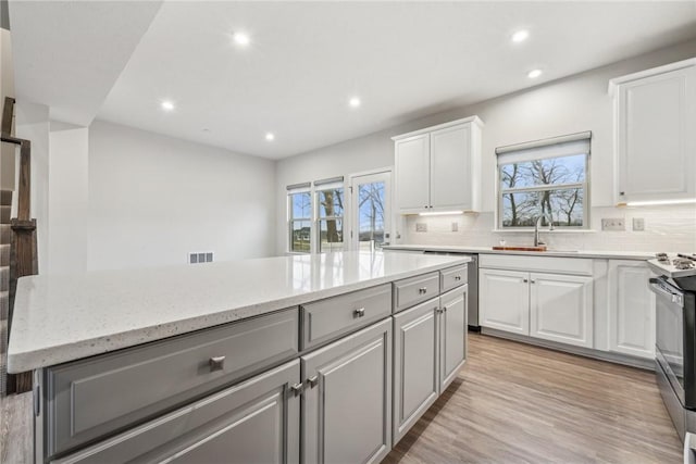 kitchen with white cabinetry, sink, a center island, backsplash, and stainless steel stove