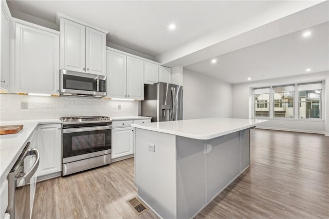 kitchen with a center island, appliances with stainless steel finishes, decorative backsplash, white cabinets, and light wood-type flooring