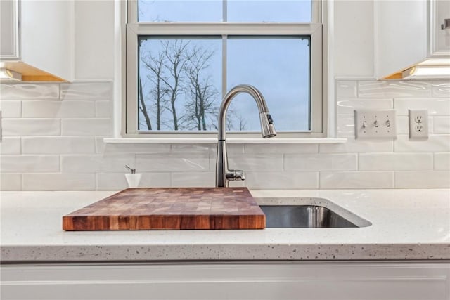 room details with white cabinets, decorative backsplash, and light stone counters