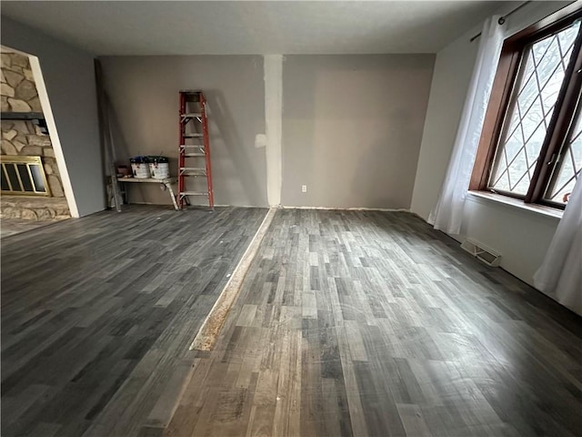 unfurnished living room featuring a stone fireplace and dark wood-type flooring