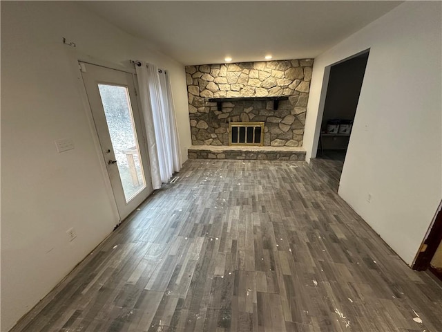 unfurnished living room featuring a healthy amount of sunlight, a stone fireplace, and dark wood-type flooring