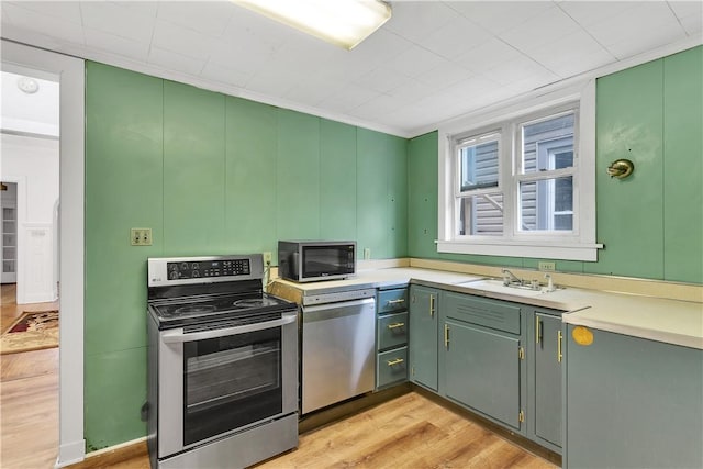 kitchen featuring sink, green cabinetry, light wood-type flooring, ornamental molding, and stainless steel appliances