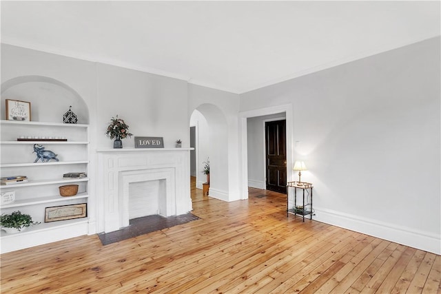 unfurnished living room featuring built in features, ornamental molding, and light wood-type flooring