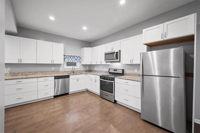 kitchen with hardwood / wood-style floors, sink, light stone counters, white cabinetry, and stainless steel appliances