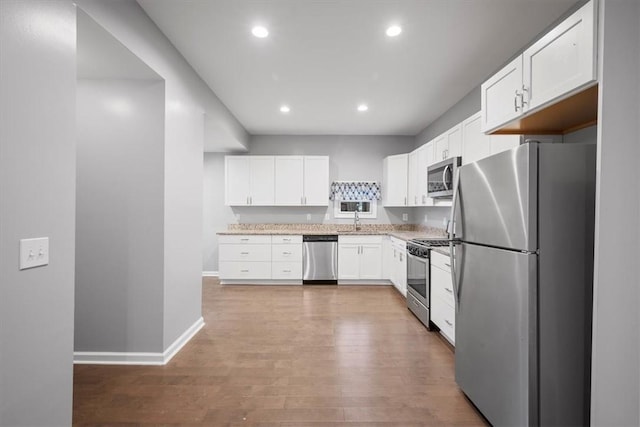 kitchen with white cabinets, sink, stainless steel appliances, and hardwood / wood-style flooring