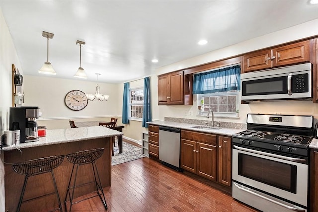 kitchen with sink, dark hardwood / wood-style flooring, pendant lighting, a breakfast bar area, and appliances with stainless steel finishes