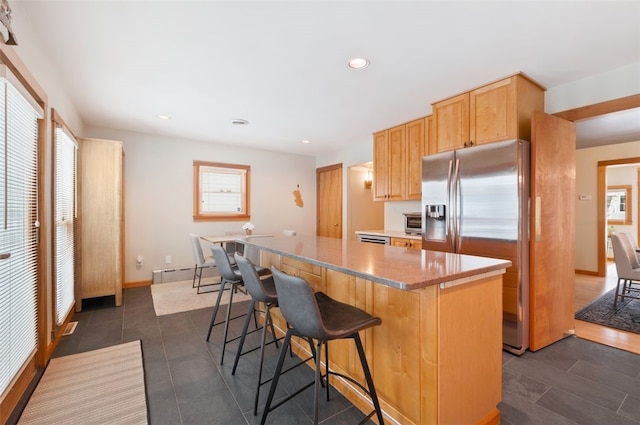 kitchen featuring a kitchen bar, stainless steel fridge, dark tile patterned floors, a kitchen island, and light stone counters