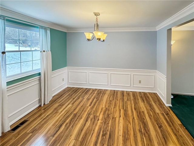 empty room featuring wood-type flooring, ornamental molding, and an inviting chandelier