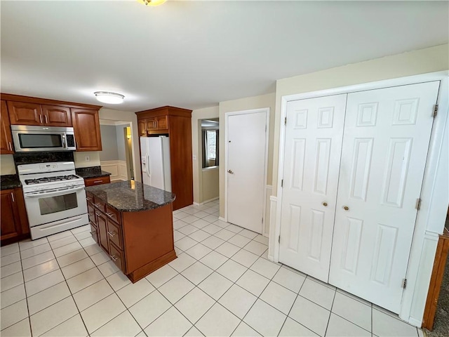 kitchen featuring a center island, light tile patterned floors, dark stone counters, and white appliances