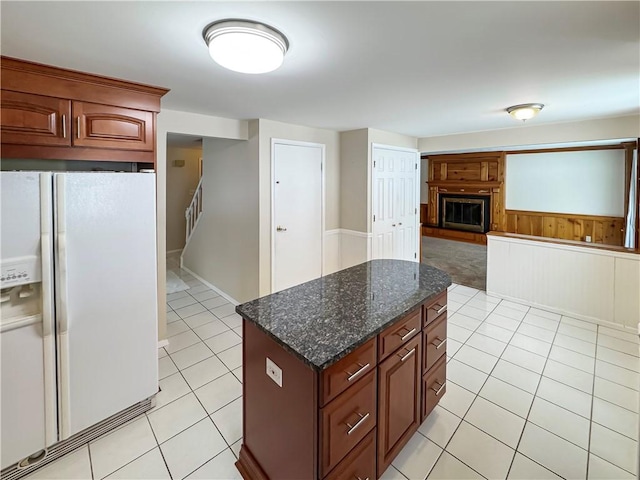 kitchen with dark stone countertops, white fridge with ice dispenser, a kitchen island, and light tile patterned floors