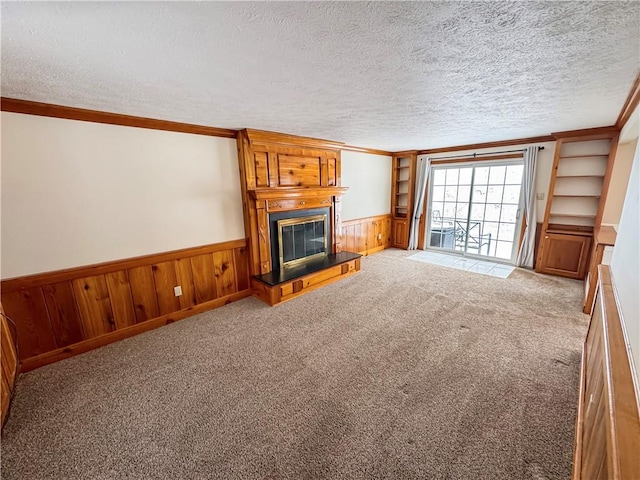 unfurnished living room featuring wooden walls, ornamental molding, a textured ceiling, a large fireplace, and light colored carpet