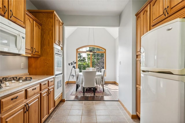 kitchen featuring lofted ceiling, light tile patterned flooring, white appliances, and hanging light fixtures