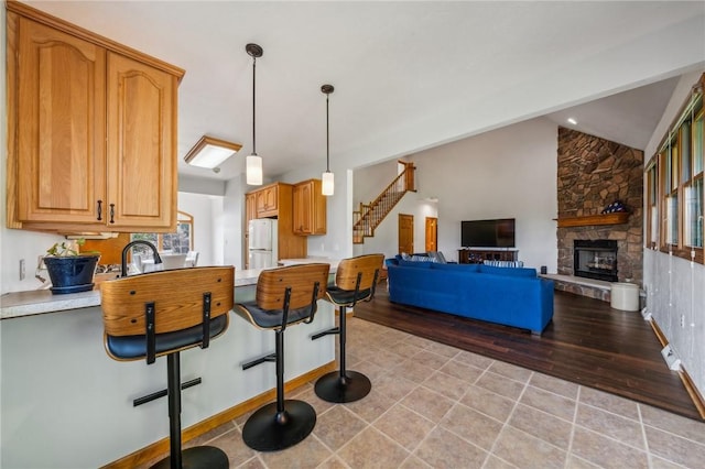 kitchen with vaulted ceiling, a fireplace, white fridge, hanging light fixtures, and a breakfast bar area