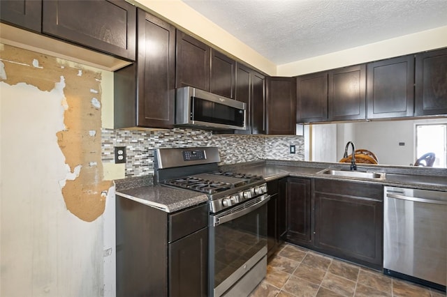 kitchen with appliances with stainless steel finishes, backsplash, dark brown cabinets, a textured ceiling, and sink