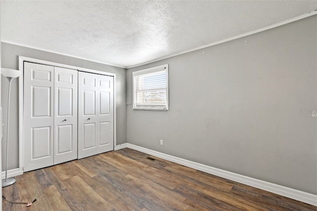 unfurnished bedroom featuring a closet, dark hardwood / wood-style flooring, crown molding, and a textured ceiling