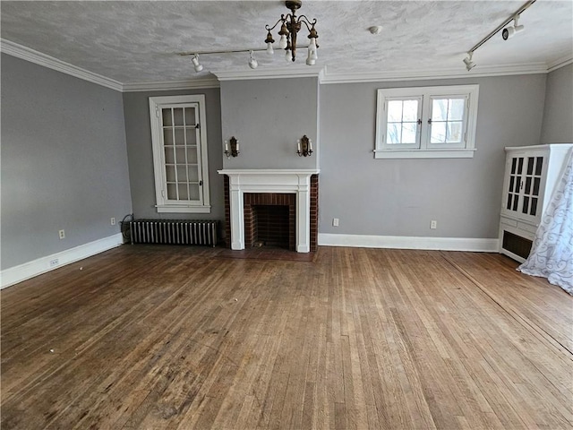 unfurnished living room featuring radiator heating unit, rail lighting, ornamental molding, and a brick fireplace