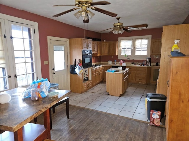 kitchen featuring stainless steel gas stovetop, a center island, ceiling fan, light tile patterned floors, and black oven