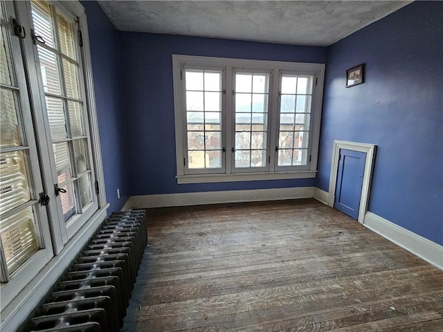 spare room featuring dark hardwood / wood-style flooring, a textured ceiling, and radiator