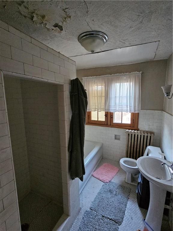 bathroom with radiator heating unit, toilet, tile walls, and independent shower and bath