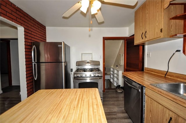 kitchen featuring appliances with stainless steel finishes, dark hardwood / wood-style flooring, brick wall, ceiling fan, and butcher block counters