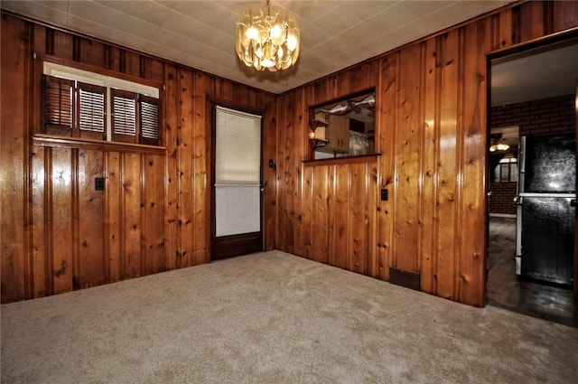 empty room featuring wooden walls, carpet, and an inviting chandelier