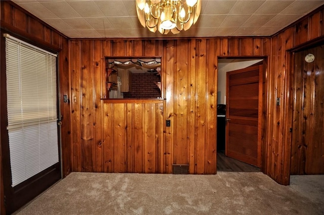 unfurnished room with dark colored carpet, a notable chandelier, and wood walls