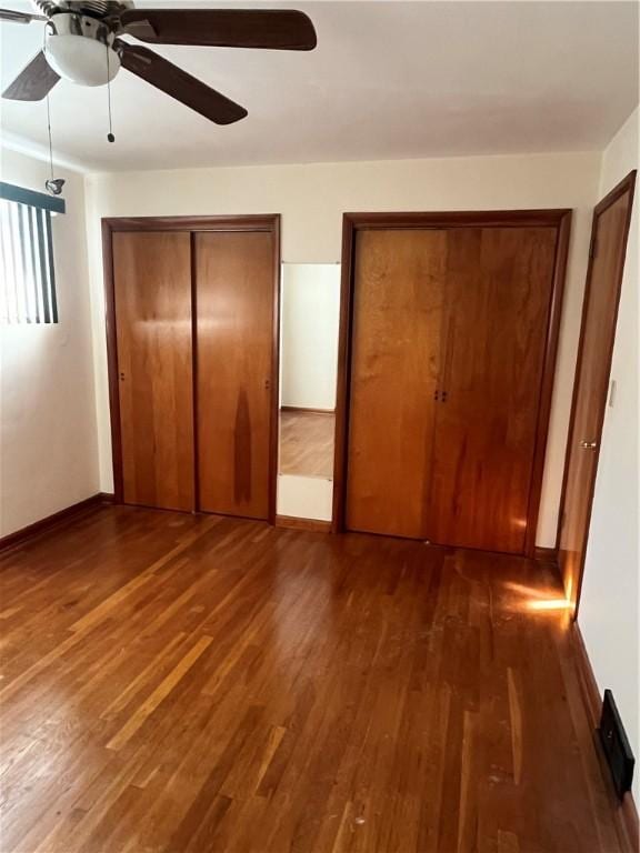 unfurnished bedroom with dark hardwood / wood-style flooring, two closets, and ceiling fan