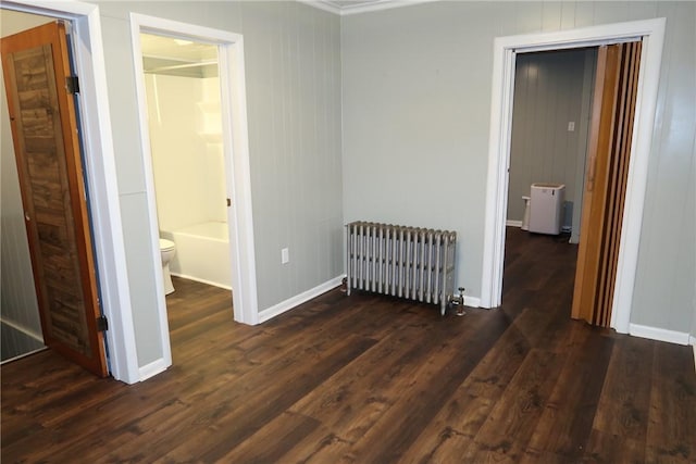 unfurnished bedroom featuring radiator heating unit, ensuite bathroom, and dark wood-type flooring