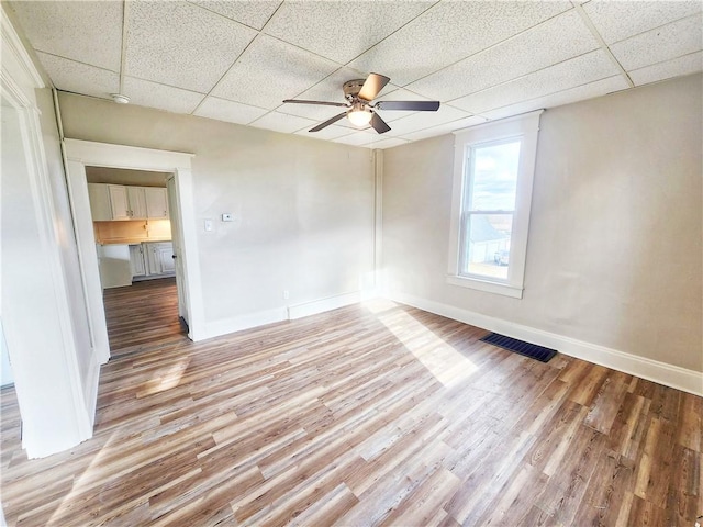 empty room with ceiling fan, a drop ceiling, and light wood-type flooring