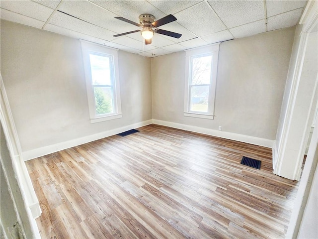 empty room featuring a paneled ceiling, light hardwood / wood-style floors, and a wealth of natural light