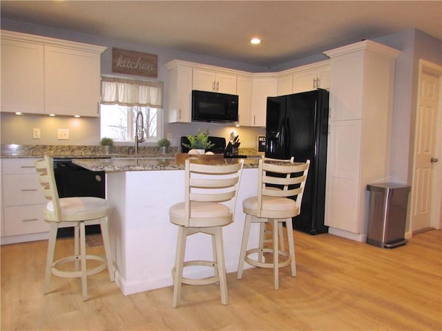 kitchen with a center island, black appliances, white cabinets, light hardwood / wood-style flooring, and a breakfast bar area