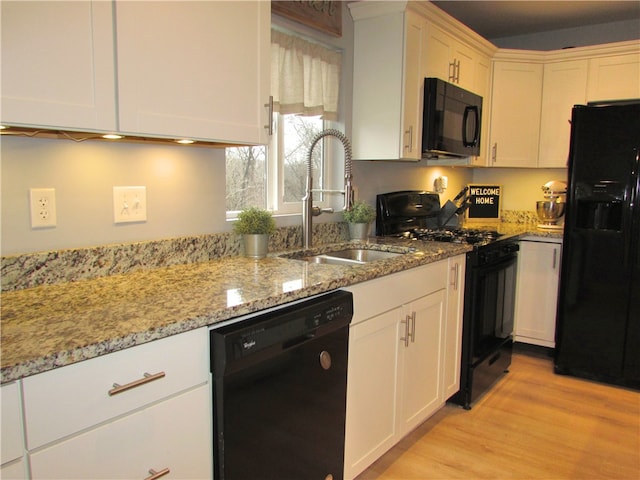 kitchen with light stone countertops, white cabinetry, sink, light hardwood / wood-style floors, and black appliances