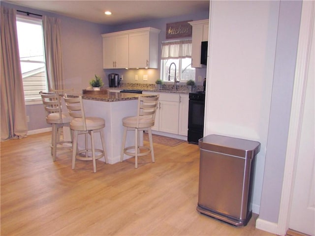 kitchen with white cabinets, a kitchen breakfast bar, electric range, dark stone countertops, and a kitchen island