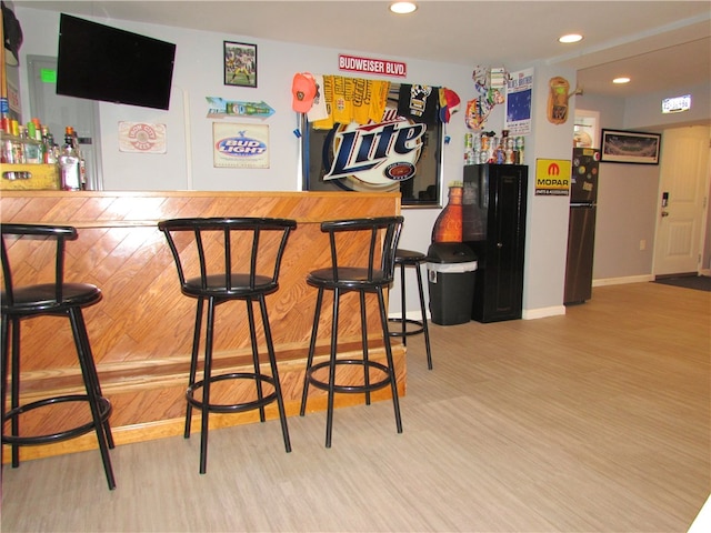 bar with light wood-type flooring and stainless steel refrigerator