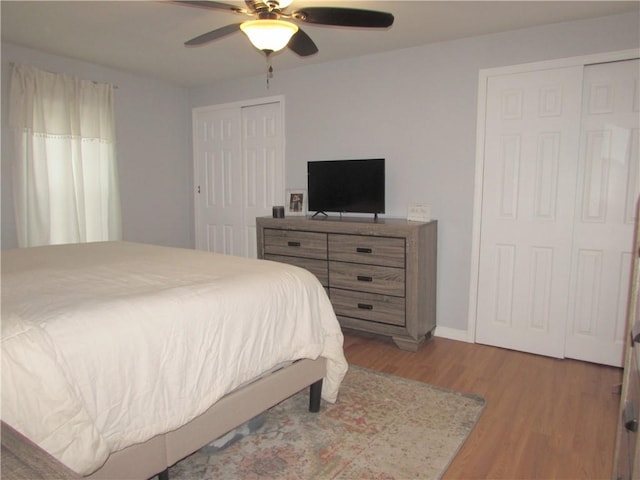 bedroom featuring hardwood / wood-style flooring, ceiling fan, and multiple closets