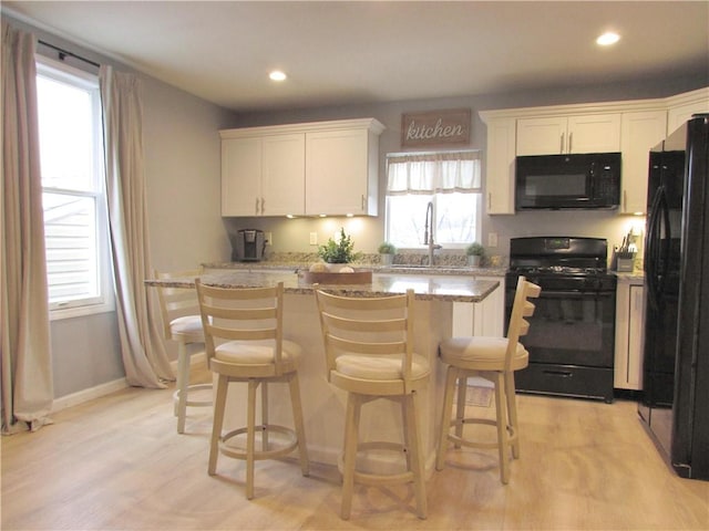 kitchen with sink, black appliances, white cabinets, a kitchen island, and plenty of natural light