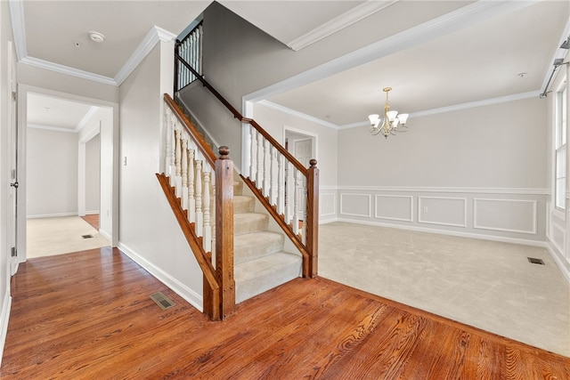 staircase featuring hardwood / wood-style floors, ornamental molding, and an inviting chandelier