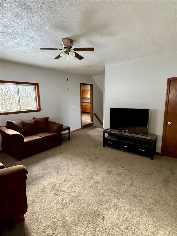 living room with ceiling fan, carpet floors, and a textured ceiling