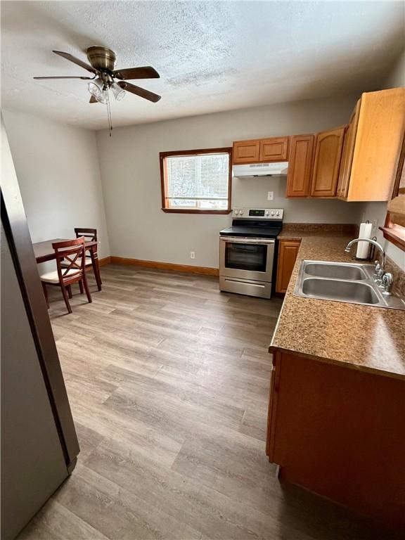 kitchen featuring a textured ceiling, ceiling fan, stainless steel electric stove, sink, and light hardwood / wood-style floors