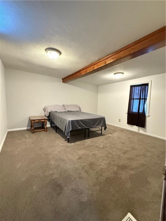 bedroom with dark colored carpet, a textured ceiling, and beamed ceiling