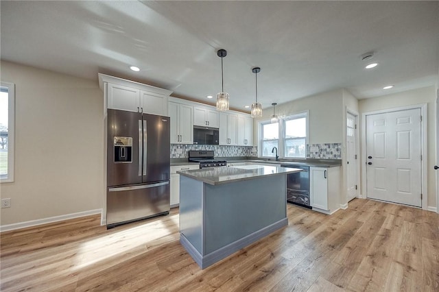 kitchen with a center island, white cabinets, hanging light fixtures, light wood-type flooring, and stainless steel appliances