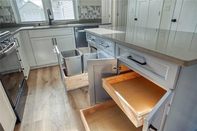 kitchen featuring dishwasher, sink, light hardwood / wood-style flooring, backsplash, and stove